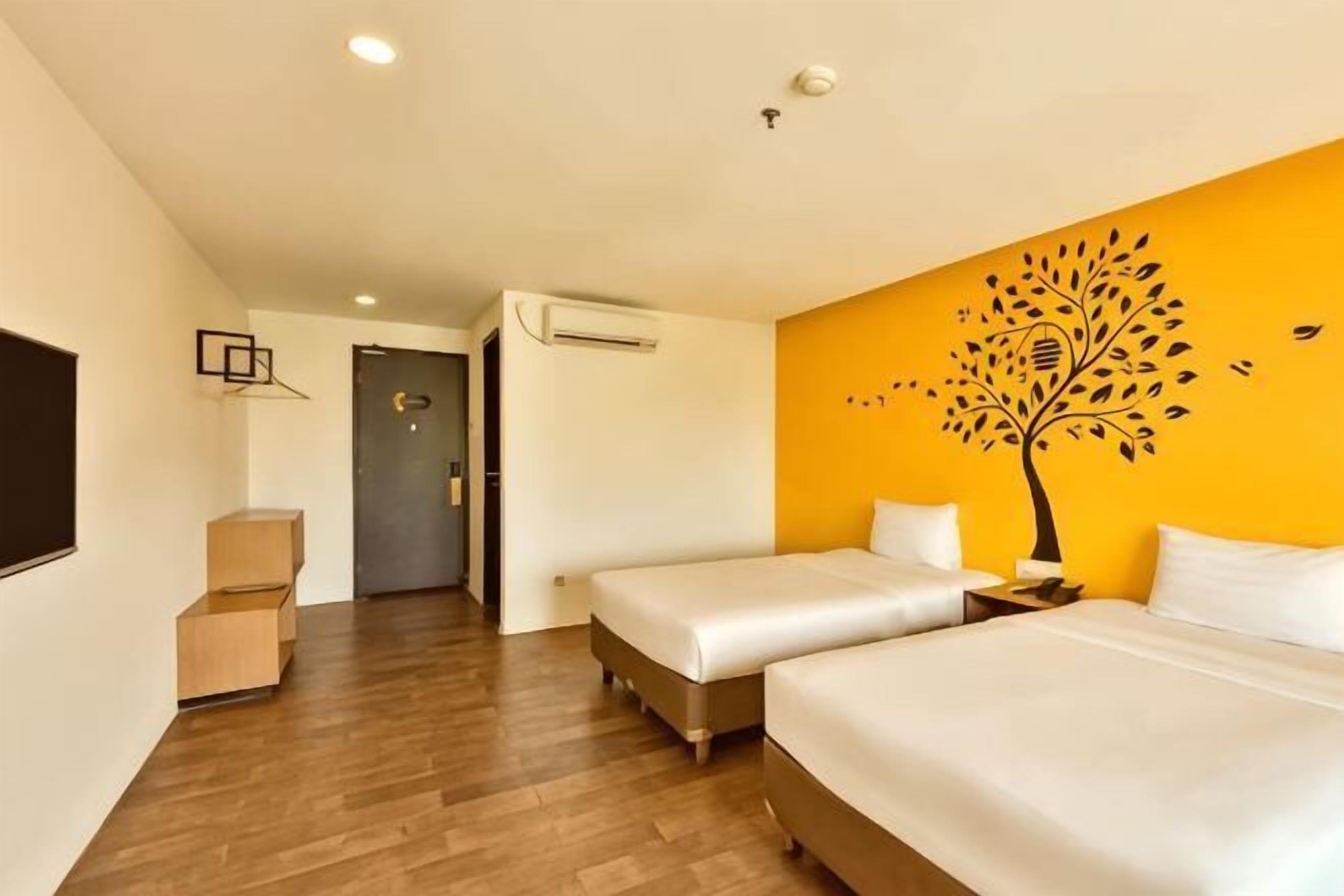A hotel room with two beds, a wooden floor, a wall-mounted air conditioner, and a door leading to another room.