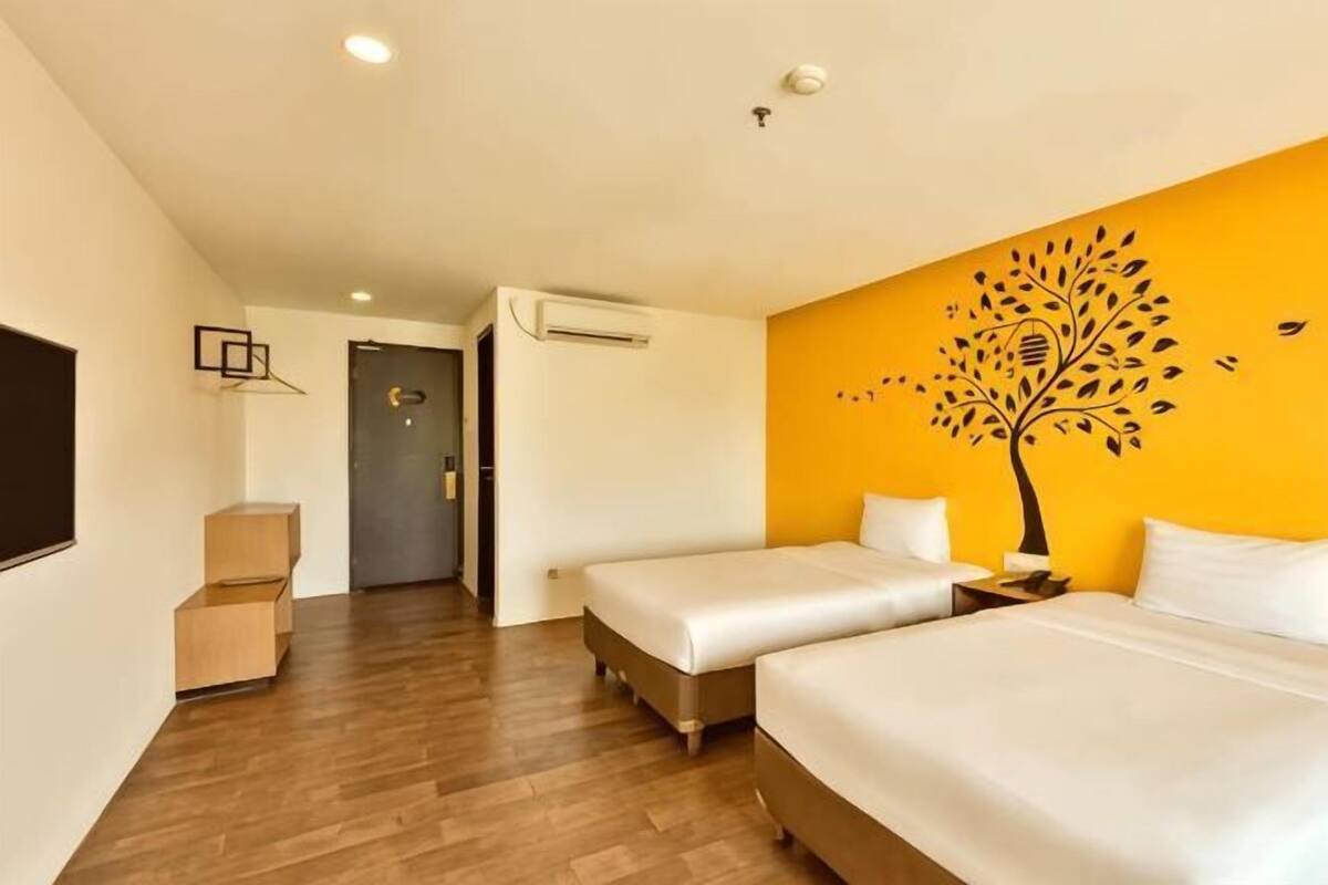 Quarto de hotel com duas camas, piso de madeira, ar condicionado fixado na parede e porta que dá para outro cômodo.
