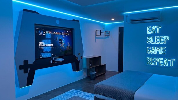 Un dormitorio moderno con una configuración de juegos, una cama y un letrero motivacional en la pared.