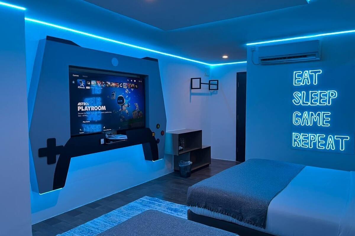 Quarto moderno com espaço para jogos, uma cama e um letreiro motivacional na parede.