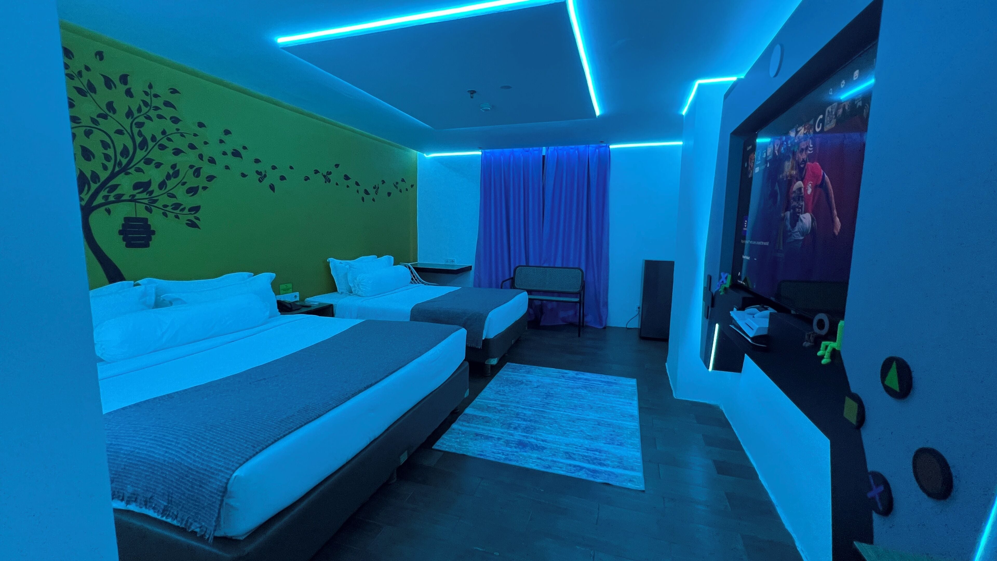 Una habitación de hotel con dos camas, un televisor de pantalla plana y una pared verde con un adhesivo de un árbol.