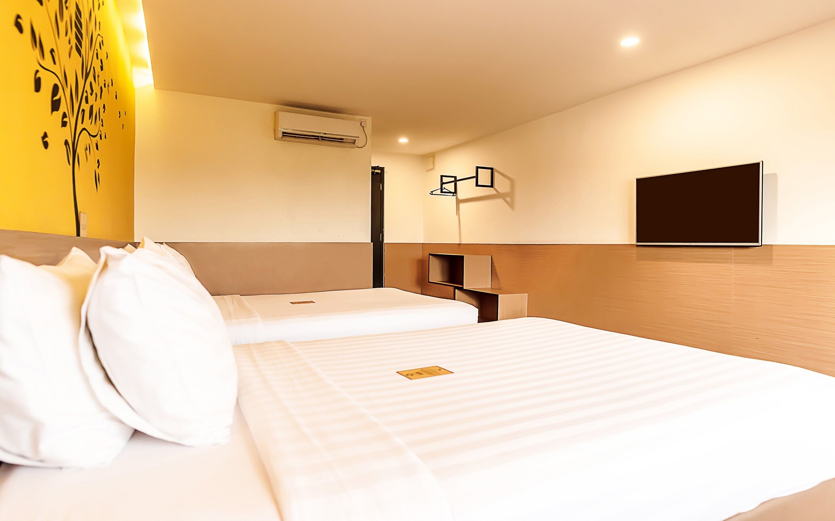 A hotel room with two beds, a mounted TV, and an air conditioning unit on the wall.