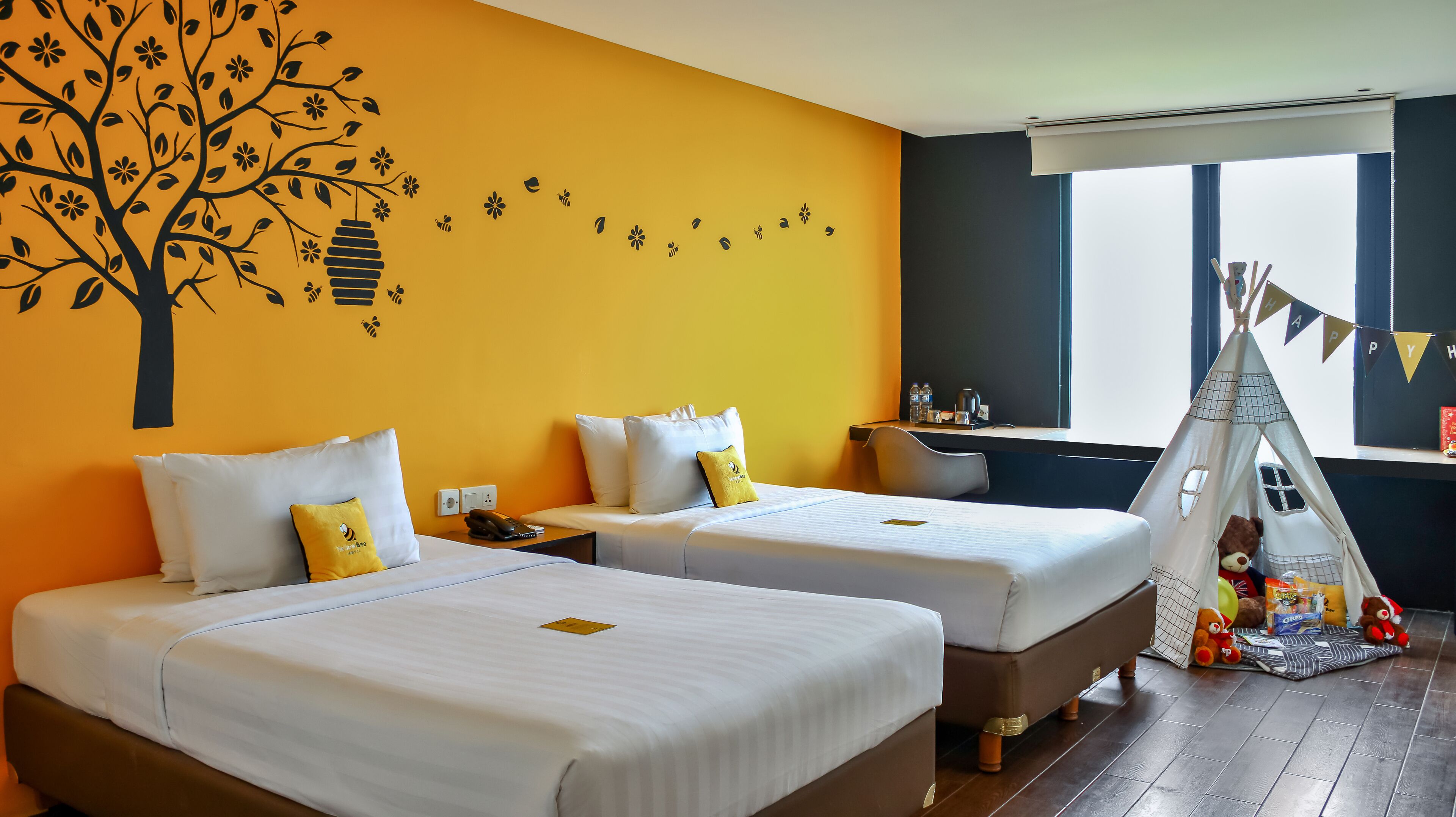Ein Hotelzimmer mit zwei Betten, einer Wanddekoration mit Baummotiv, einem Fenster mit Blick und einer Tipi-Dekoration.