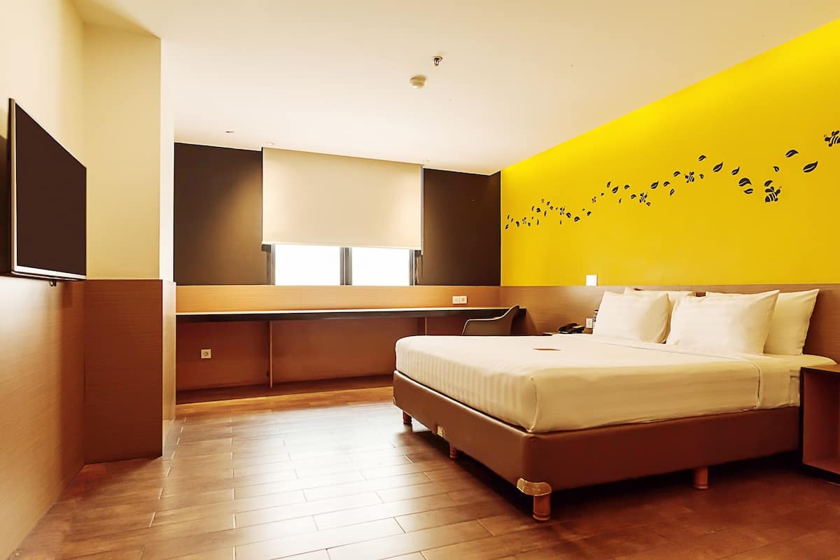 Quarto de hotel moderno com uma cama grande, uma escrivaninha e uma parede de destaque amarelo vibrante.