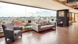 Amplia sala de estar con un gran ventanal que ofrece vistas a la ciudad, un sofá gris, un sillón gris y una pequeña mesa auxiliar.