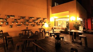 Un comedor interior con varias mesas y sillas de madera, plantas en macetas en las paredes e iluminación cálida.