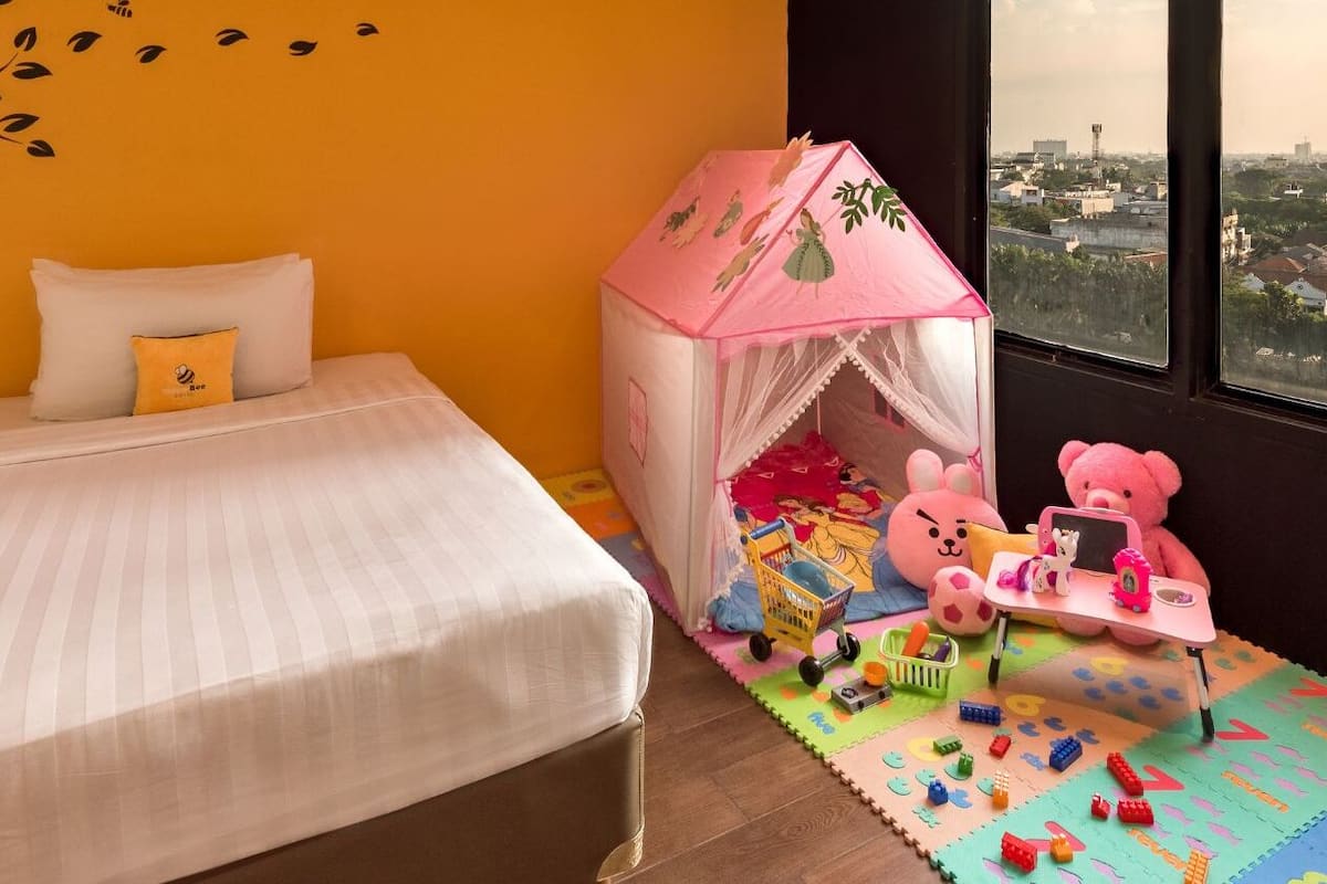 Quarto com cama, uma pequena tenda, brinquedos e vista para a cidade.