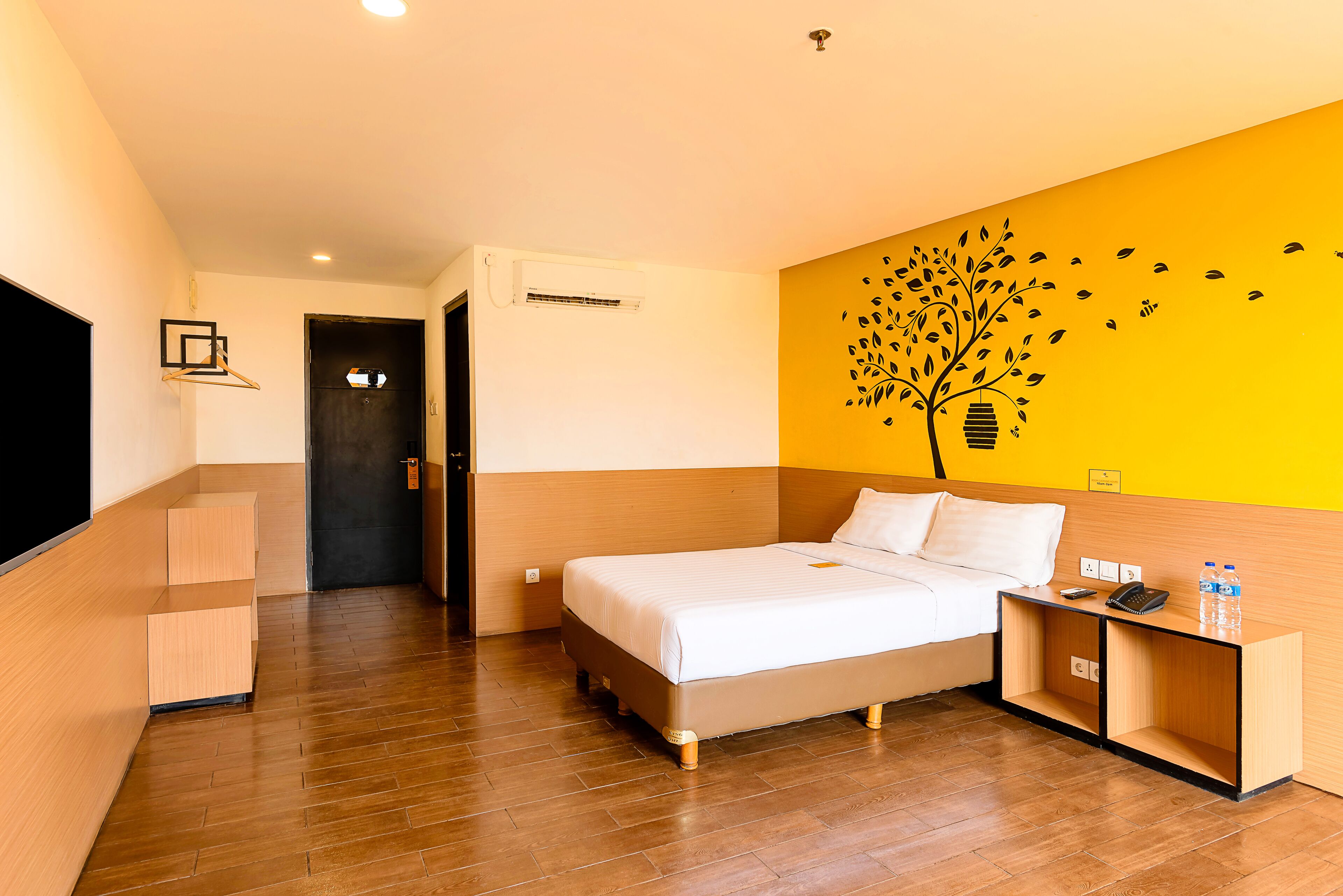 A hotel room with a bed, bedside table, and a wall with a tree decal.