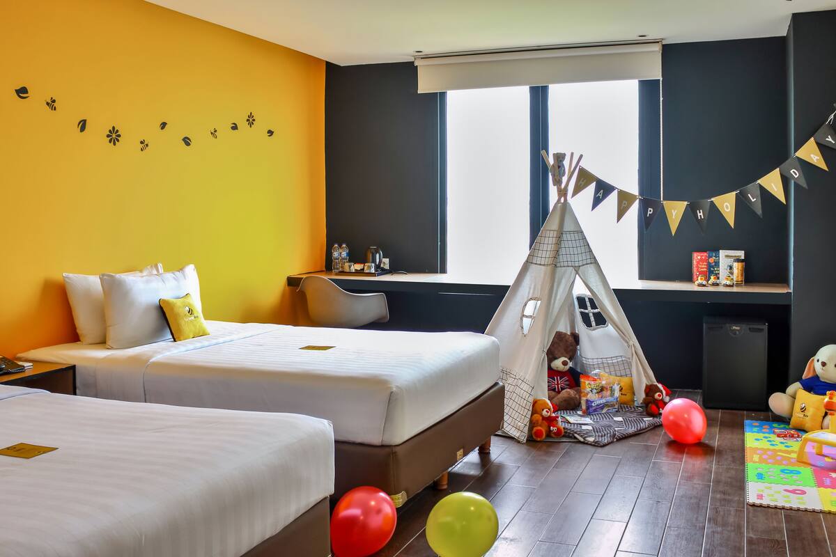 Quarto de hotel com duas camas, uma escrivaninha, uma janela, um urso de pelúcia e um tipi.