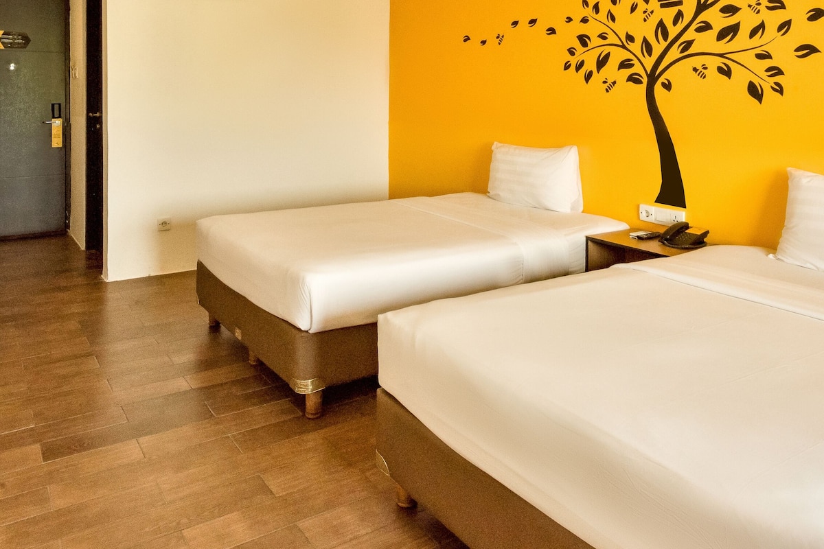 Quarto de hotel com duas camas, piso de madeira, parede com decalque de árvore e porta com fechadura.