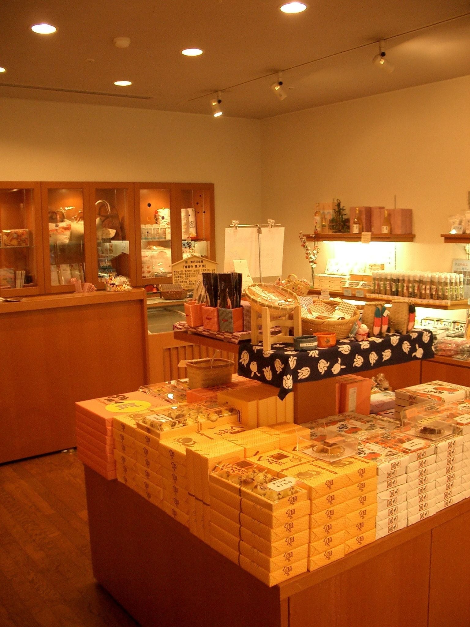 A store interior with shelves stocked with various items, a display counter with boxed products, and wooden cabinets.