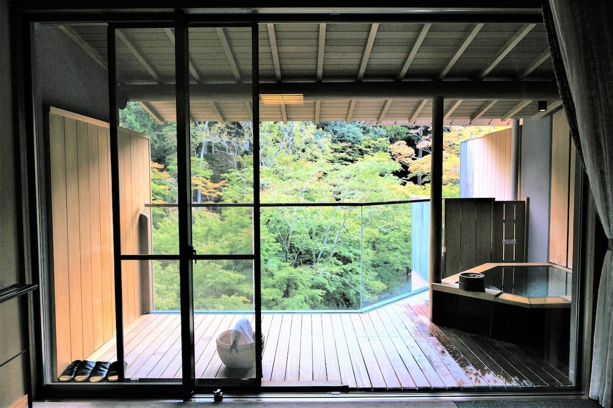 Una habitación con un ventanal grande, una terraza de madera, una bañera y una mesita.