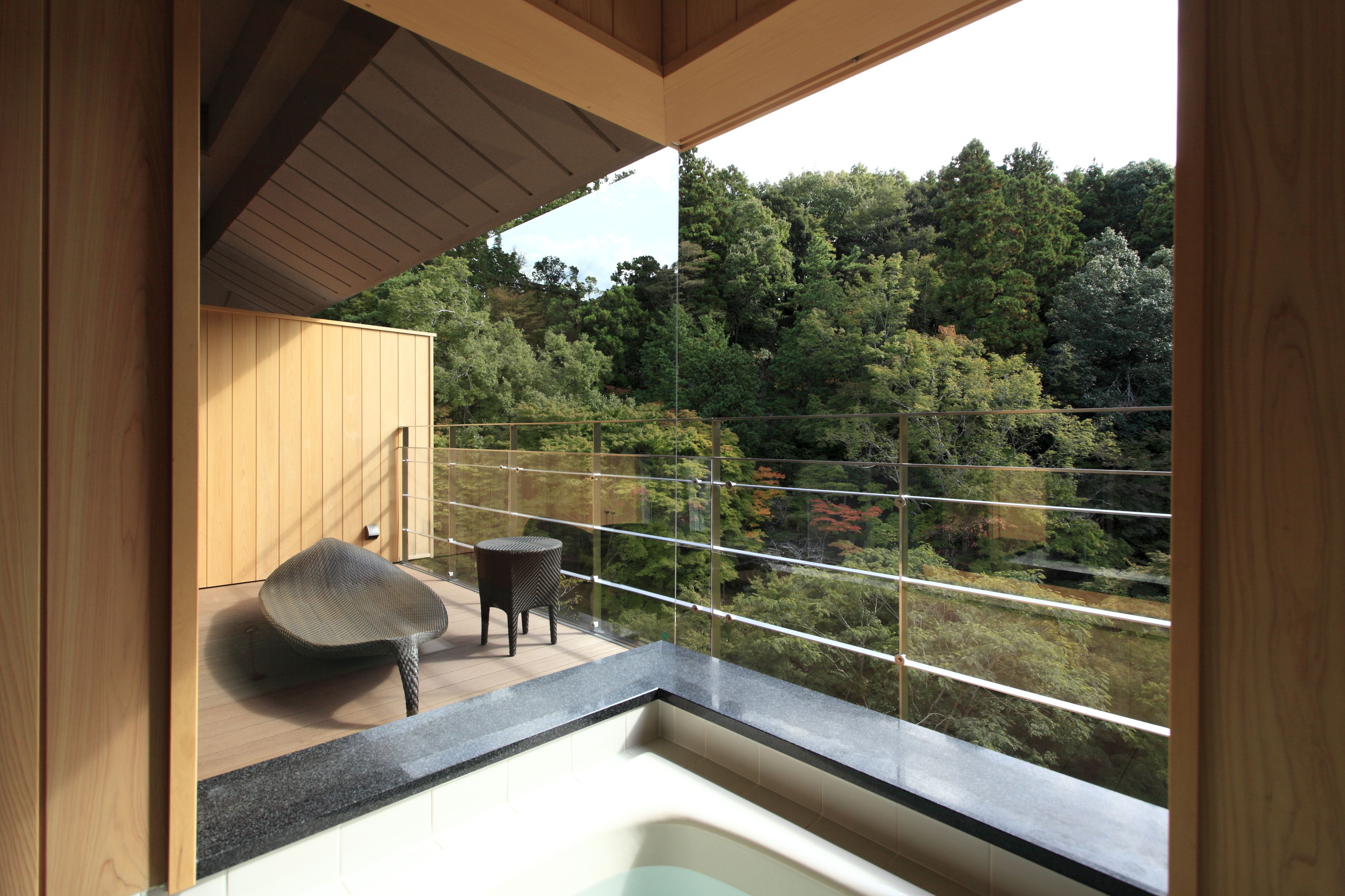 A balcony with a view of a forest, a small round table, and a chair.