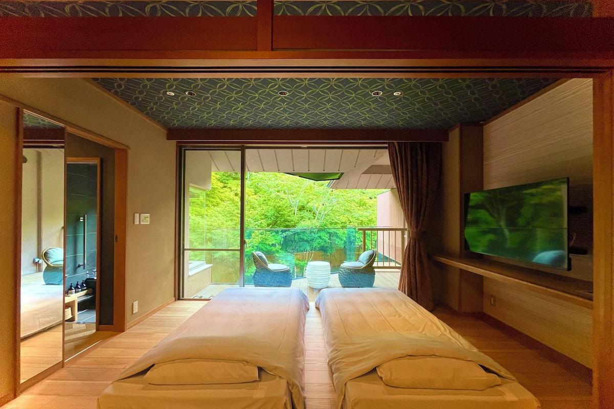 Un dormitorio con una cama grande, televisión y puerta corrediza de vidrio que da a un balcón con mobiliario exterior.