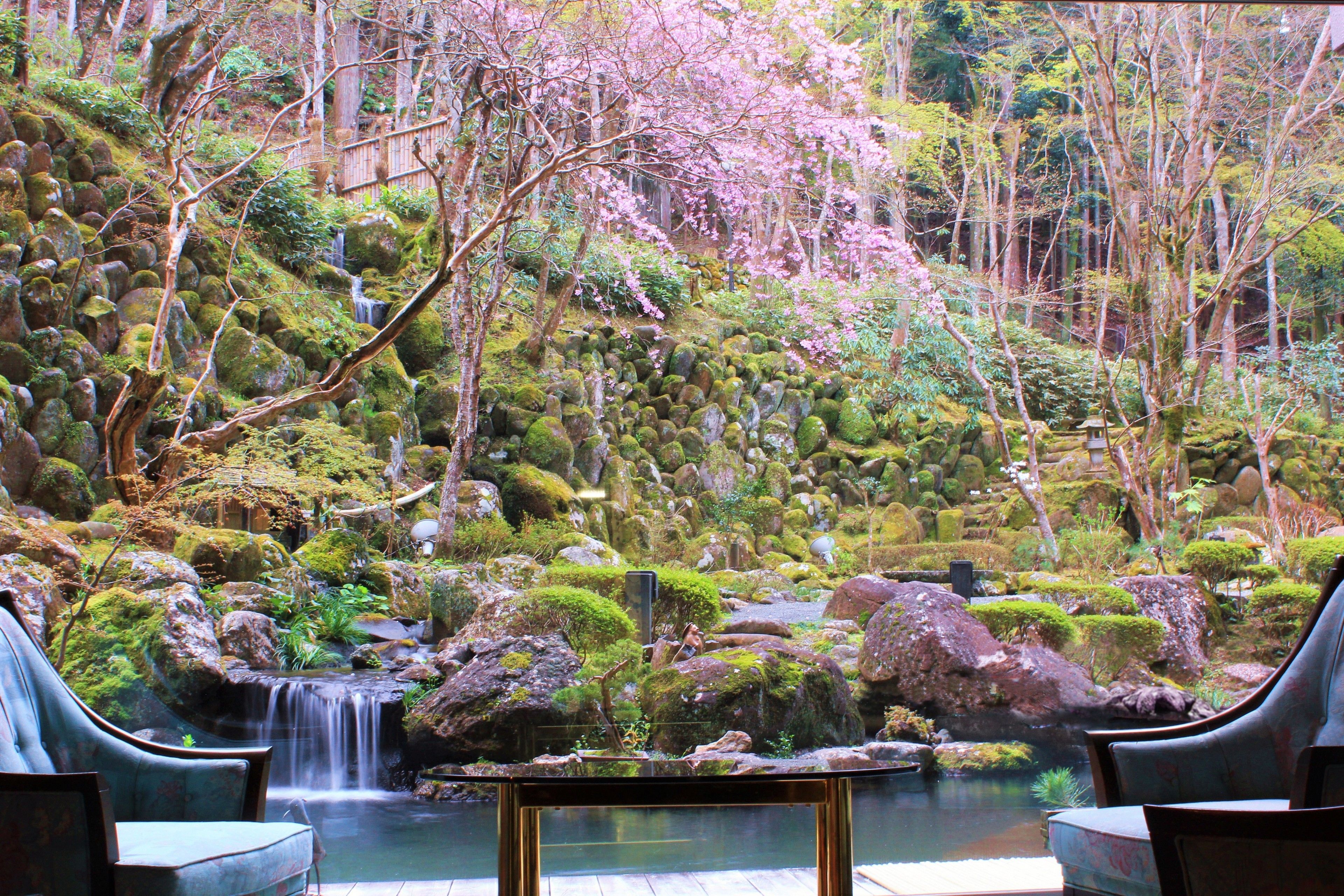 A serene indoor garden with a small waterfall, seating areas, and a pond.
