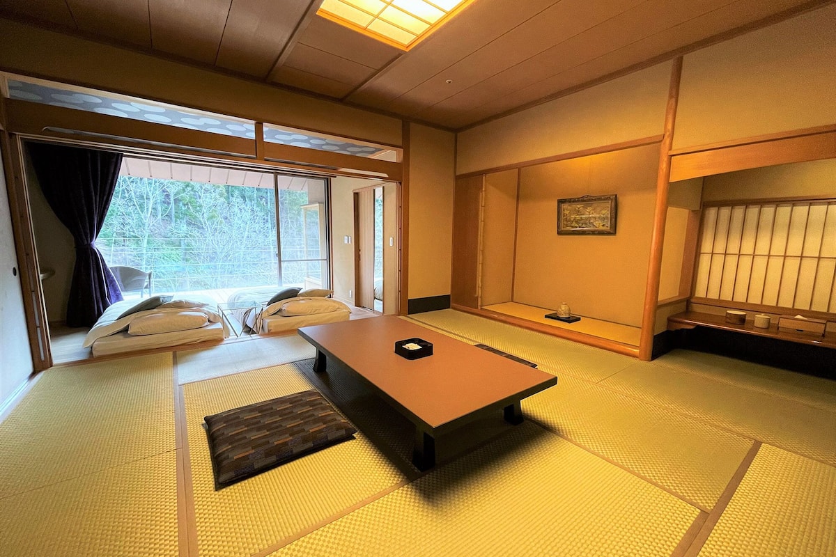 Una habitación con tatami, una mesa baja, un sofá y una puerta corrediza que da a un balcón.