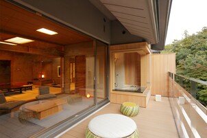 Un área de spa moderna con una sala acristalada, terraza de madera y vistas al bosque circundante.