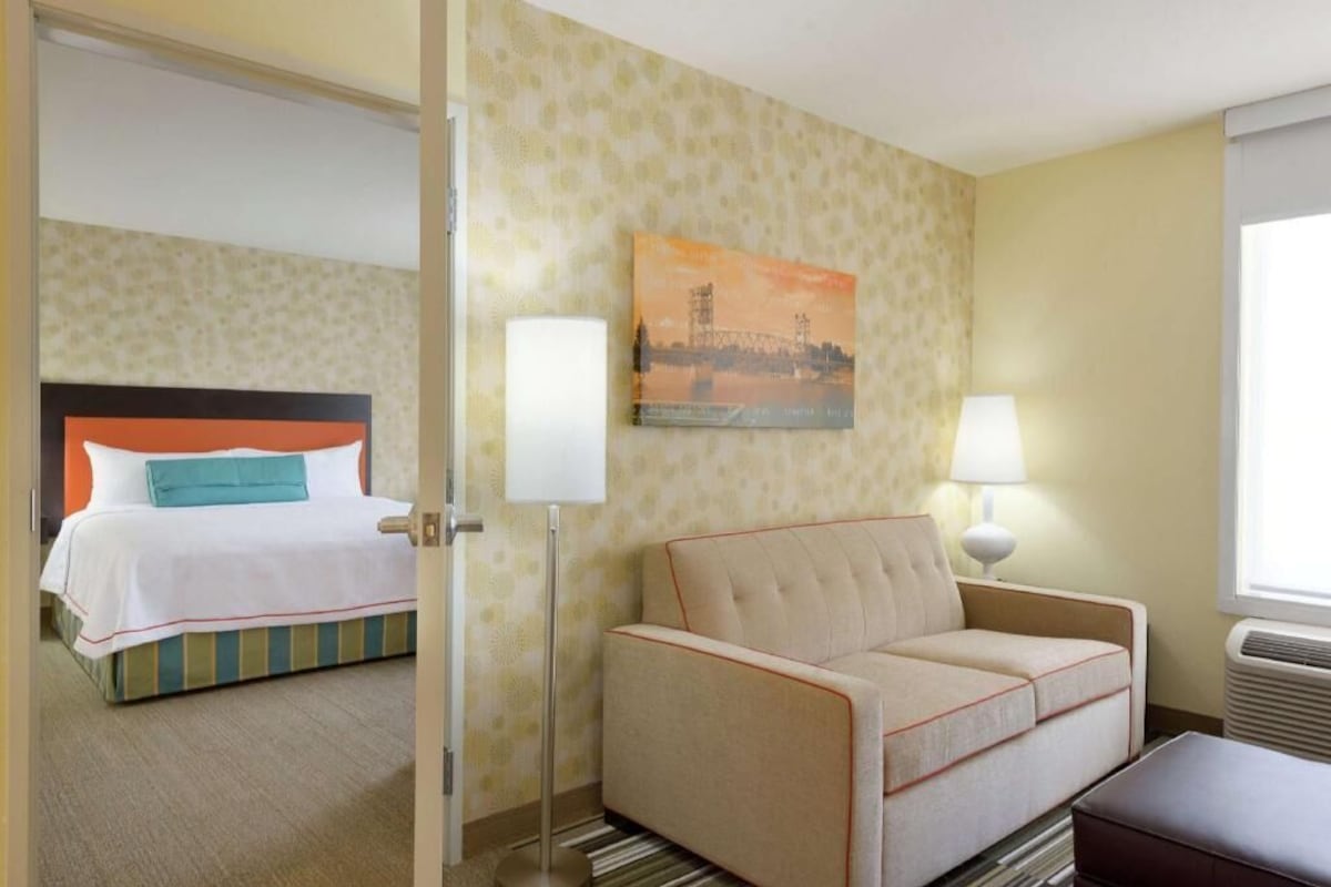 Une chambre d’hôtel avec un lit, un canapé, une lampe, un tableau et une fenêtre.