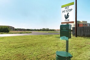 A pet waste station with a sign indicating a pet pit stop, a green trash bin, and a building in the background. - Home2 Suites by Hilton Alexandria (Alexandria)