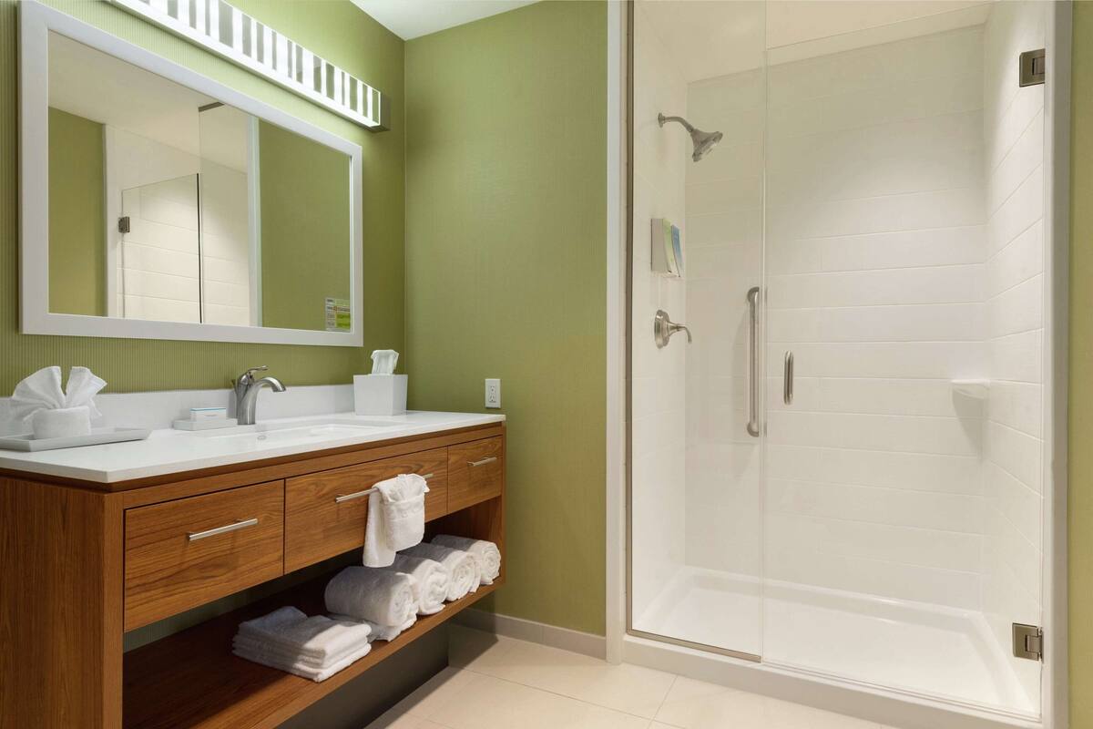 Un baño con tocador de madera, un espejo grande, ducha con puerta de cristal y suelo de baldosas.