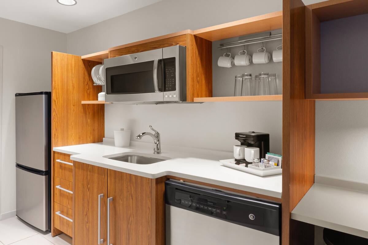 Una cocina moderna con refrigerador de acero inoxidable, microondas integrado, cafetera y armarios de madera.