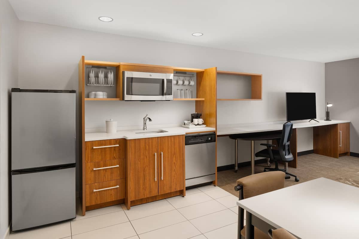 Una cocina compacta con refrigerador, microondas y lavavajillas, armarios de madera y un pequeño comedor con mesa y sillas.
