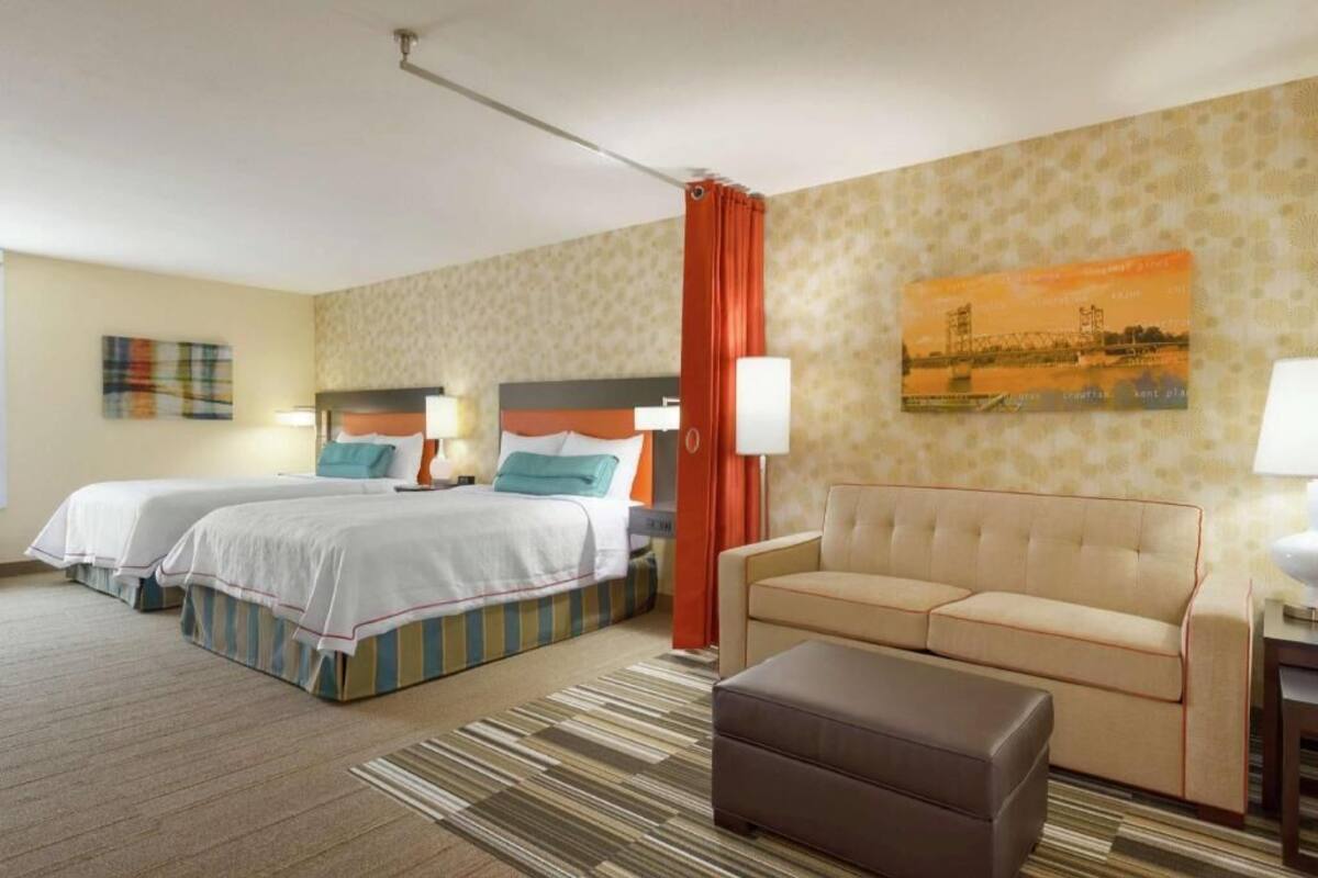 Habitación de hotel con dos camas, un sofá, una mesita y un cuadro en la pared.