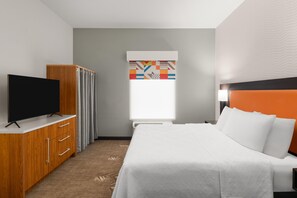 A hotel room with a bed, a TV on a wooden cabinet, a window with curtains, and a wall with a geometric pattern. - Home2 Suites by Hilton Alexandria (Alexandria)