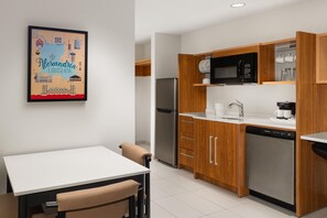 A modern kitchen with wooden cabinets, a stainless steel refrigerator, and a microwave. - Home2 Suites by Hilton Alexandria (Alexandria)