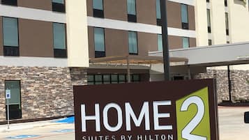 A sign for Home 2 Suites by Hilton, indicating it is a hotel with a modern design, featuring a stone facade and multiple windows.