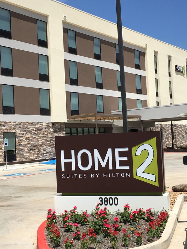 Señal de Home2 Suites by Hilton, que indica que es un hotel con diseño moderno, con fachada de piedra y múltiples ventanas.