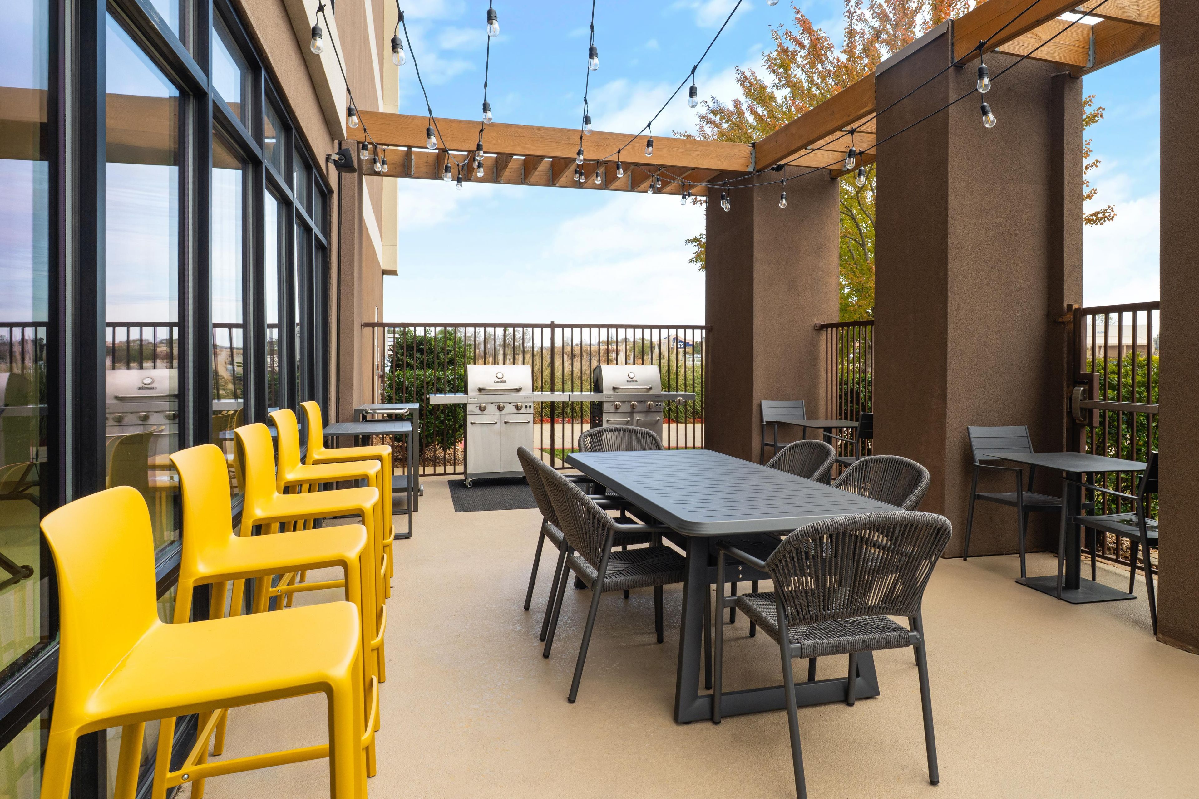 An outdoor patio with a grill, dining table, chairs, and string lights.