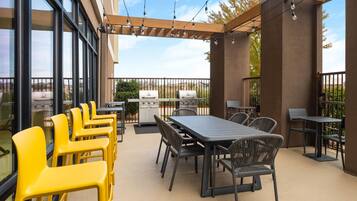 An outdoor patio with a grill, dining table, chairs, and string lights.