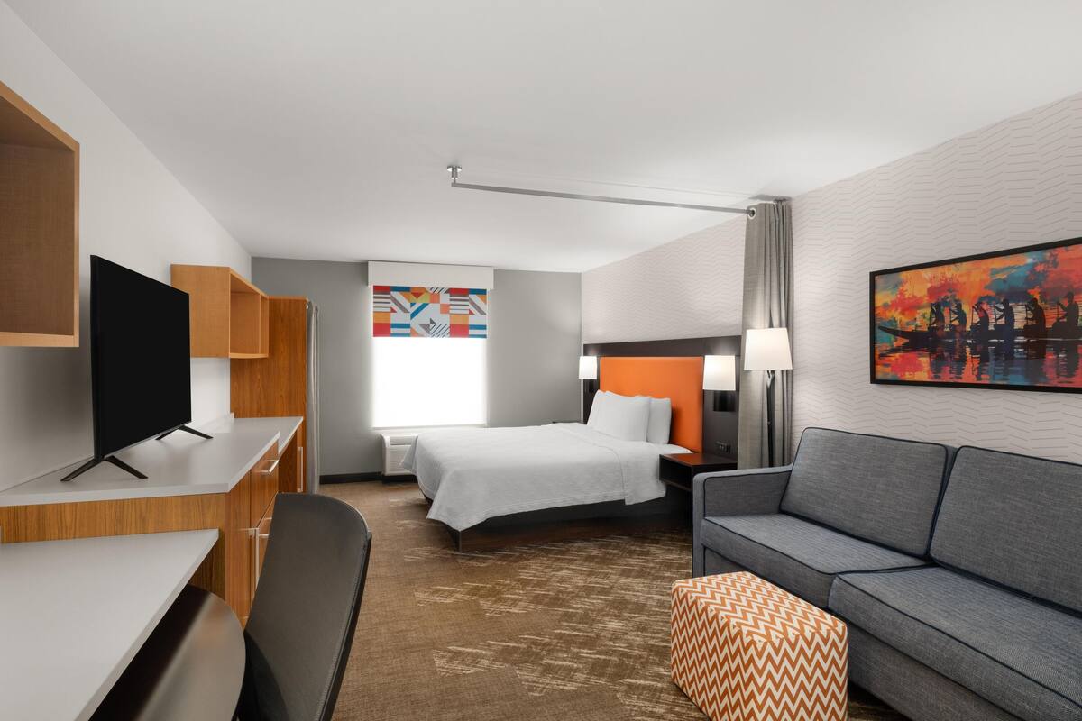 Habitación de hotel con cama, sofá, escritorio, televisor y un cuadro en la pared.