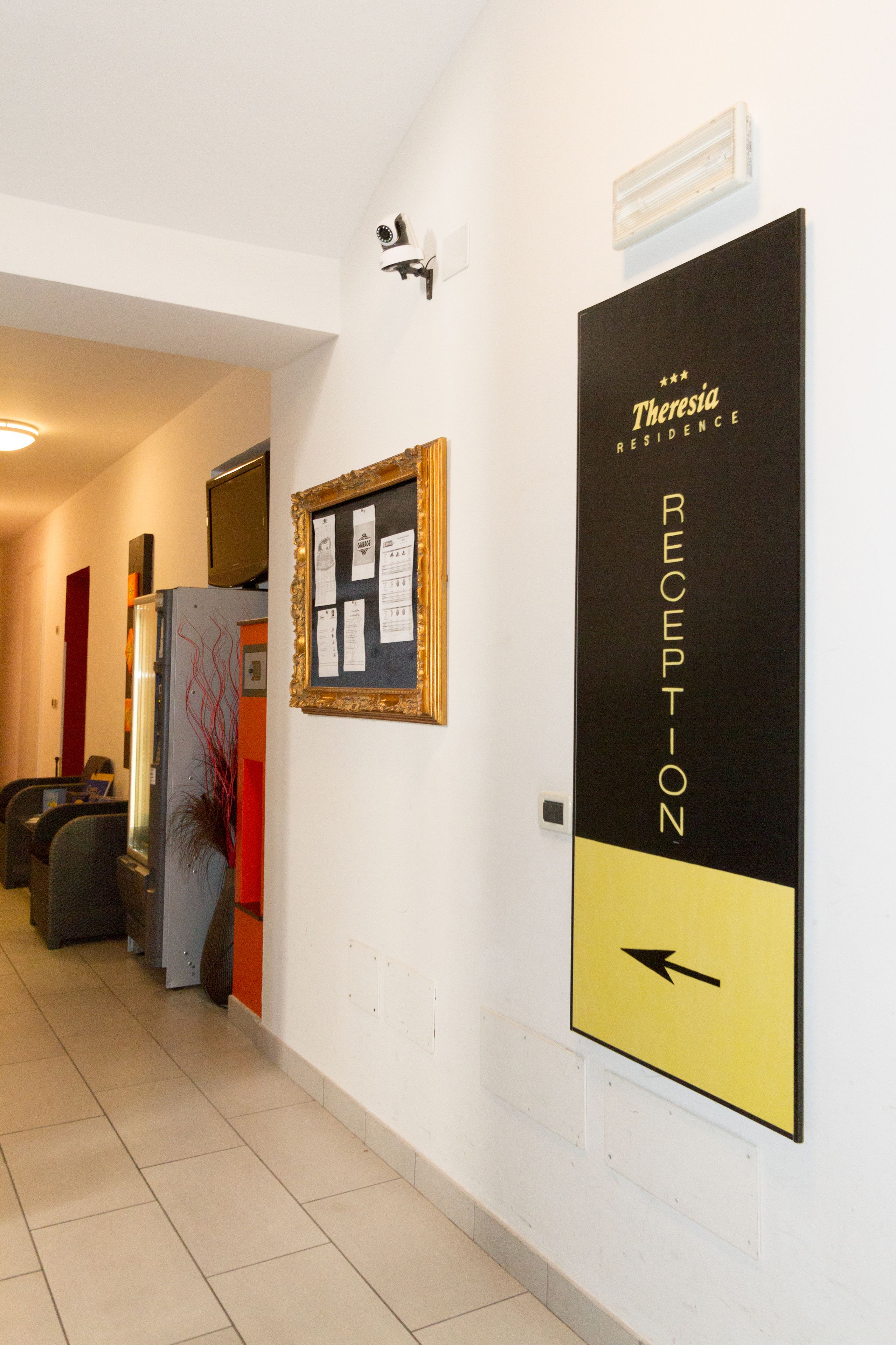 A reception area with a black and yellow sign indicating the reception, a framed notice board, and a television mounted on a cabinet.