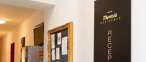A reception area with a black and yellow sign indicating the reception, a framed notice board, and a television mounted on a cabinet.