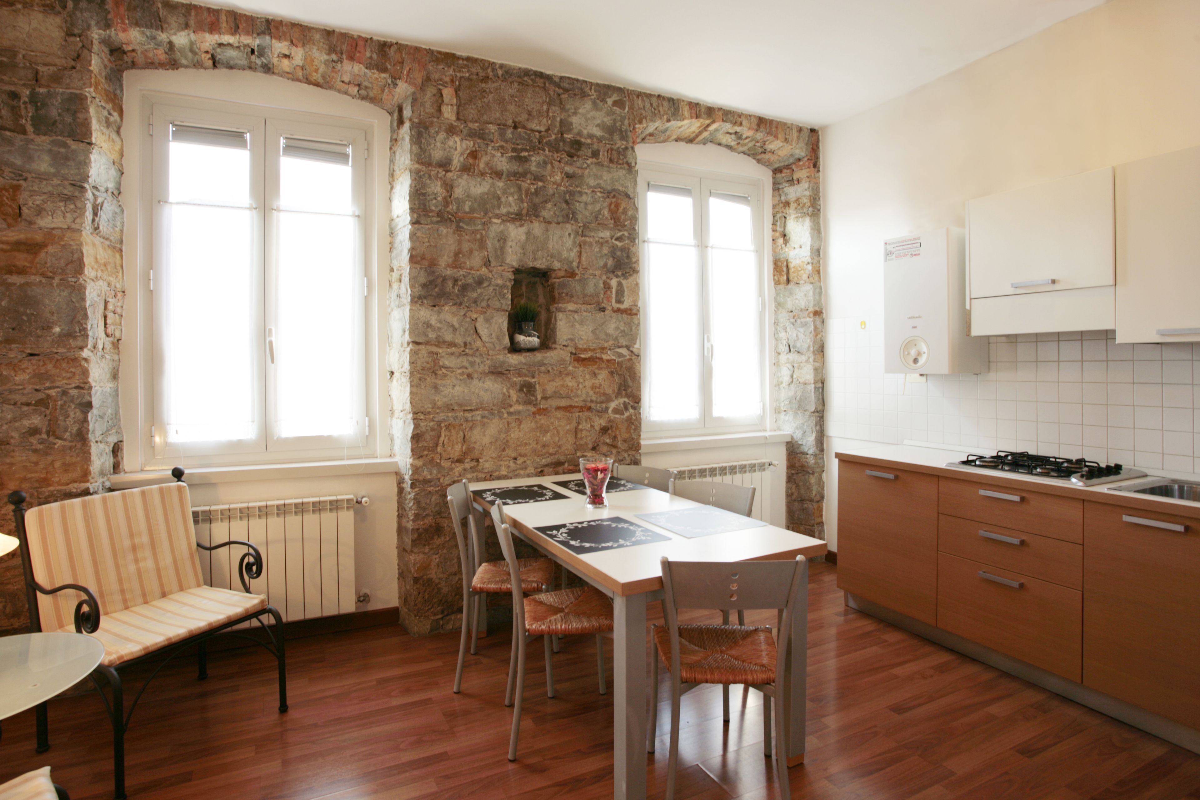 Une cuisine avec un mur en pierre, des armoires en bois et une table à manger avec des chaises.