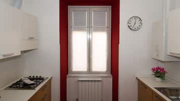A compact kitchen with a gas stove, a built-in oven, a white radiator, and a window with blinds.