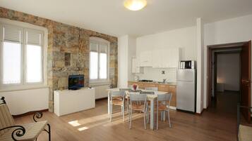 Una cucina moderna con mobili bianchi, forno a microonde integrato e frigorifero. C'è un'area pranzo con tavolo e sedie, e una parete in pietra sullo sfondo.