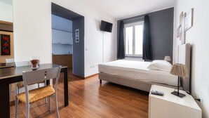 Una habitación de hotel moderna con una cama, un escritorio, una silla, un televisor y un ventanal con cortinas.