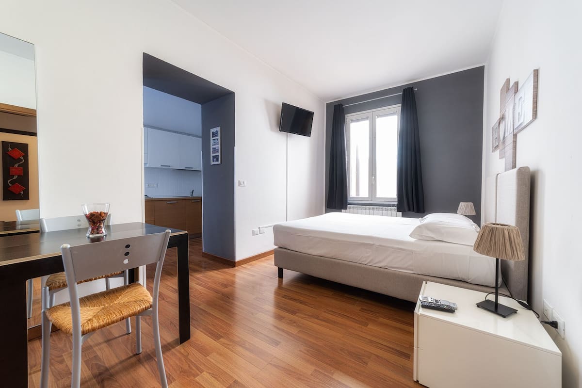 A modern hotel room with a bed, a desk, a chair, a TV, and a window with curtains.