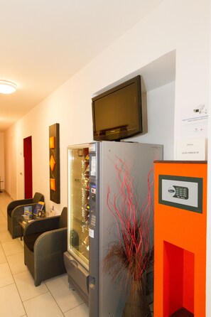 Habitación de hotel con refrigerador, televisor montado en la pared, zona de estar con sofá y sillones, y un jarrón decorativo con ramas rojas.