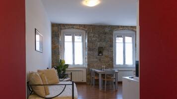 Una habitación con cama, una mesa de comedor con sillas, una pequeña cocina y una pared de piedra.