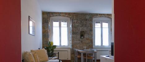 Una habitación con cama, una mesa de comedor con sillas, una pequeña cocina y una pared de piedra.