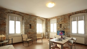 Una habitación con paredes de piedra, piso de madera, una mesa de comedor con sillas y un televisor.
