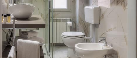 A modern bathroom with a glass shower enclosure, a marble-tiled floor, a white sink, and a toilet.