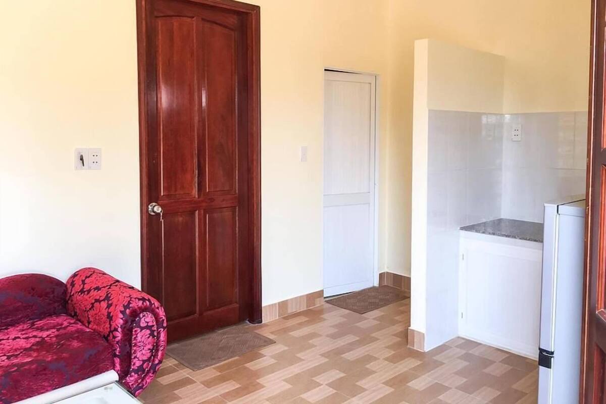 A compact kitchen with a refrigerator, a wooden door, and a patterned sofa.