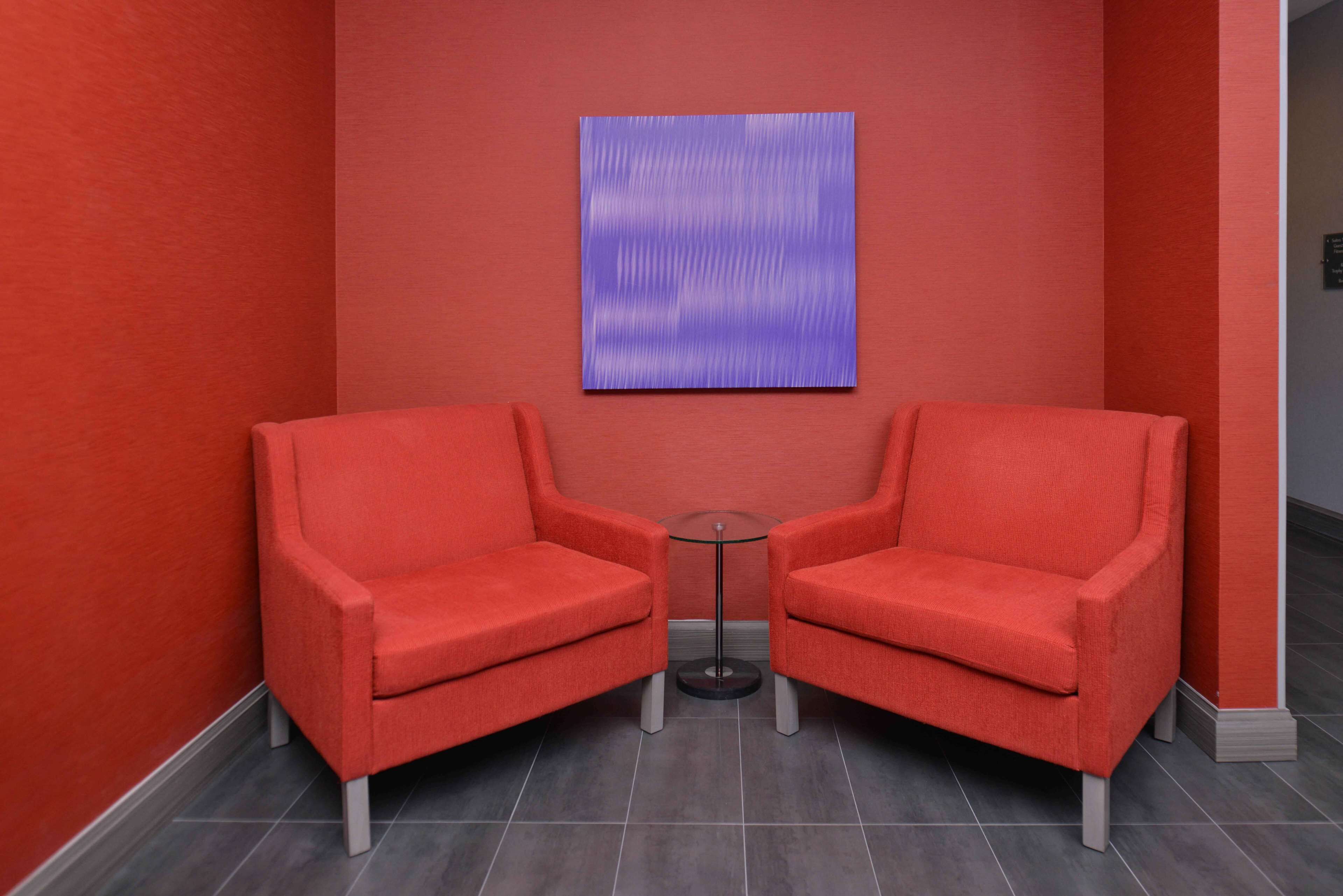 A room with two red armchairs, a small round table, and a blue abstract painting on the wall.