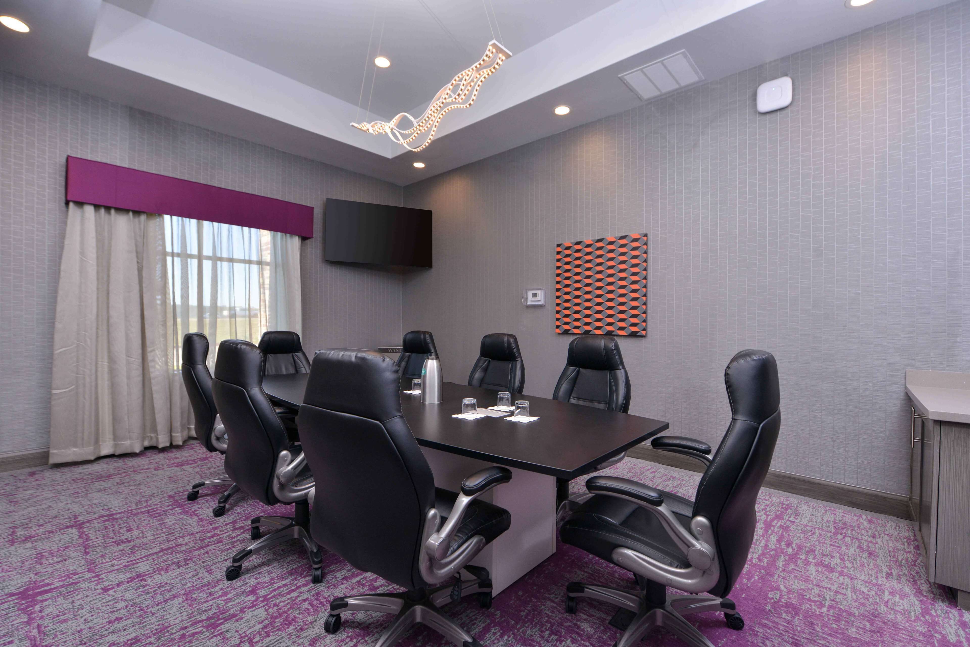 A conference room with a dark table, black chairs, a flat-screen TV, and a patterned wall decoration.