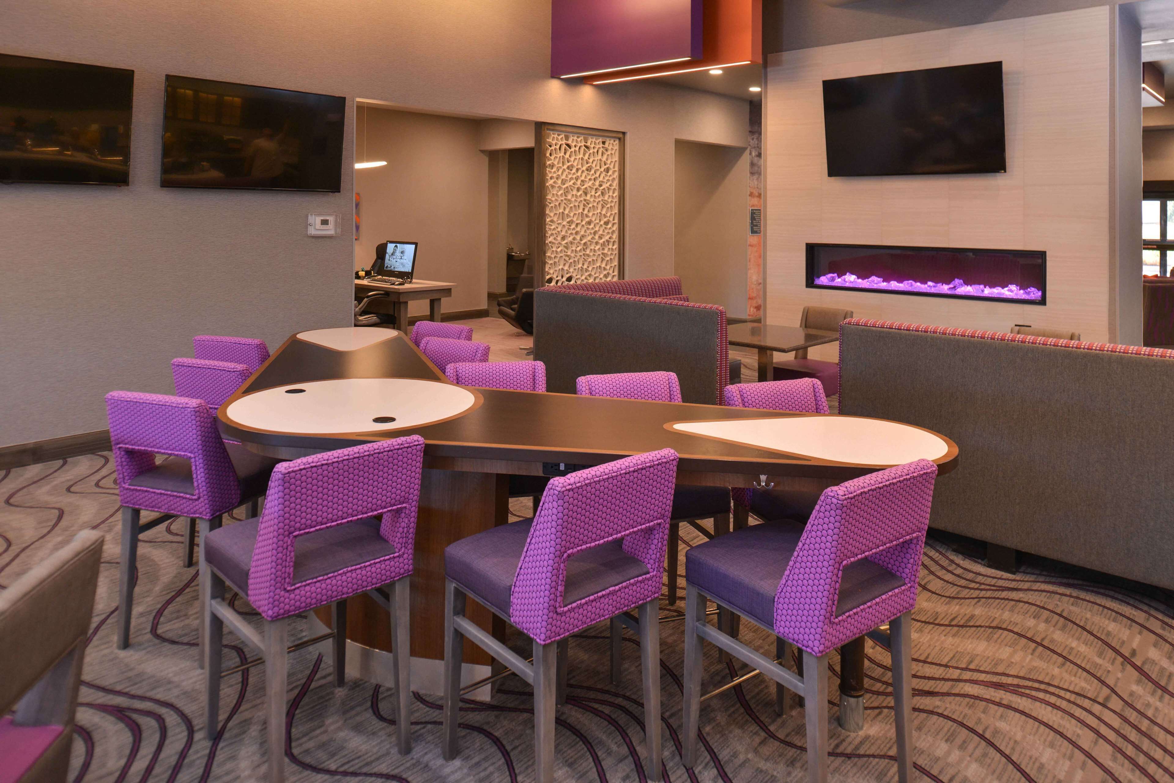 A conference room with a long table, purple chairs, a TV, and a fireplace.